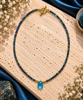Collier en perles facettées de sodalite bleu nuit et vert profond avec billes dorées et pendentif goutte d'apatite bleu lagon sur fermoir toggle doré